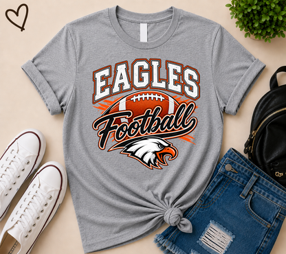 A heather gray graphic t-shirt featuring 'EAGLES Football' and an eagle head logo, styled in a flat lay with white sneakers, blue denim shorts, and a black backpack on a beige background.