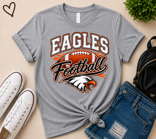 A heather gray graphic t-shirt featuring 'EAGLES Football' and an eagle head logo, styled in a flat lay with white sneakers, blue denim shorts, and a black backpack on a beige background.